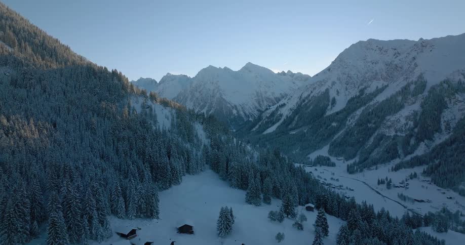 Snow covers buildings and conifer forest on mountain slopes