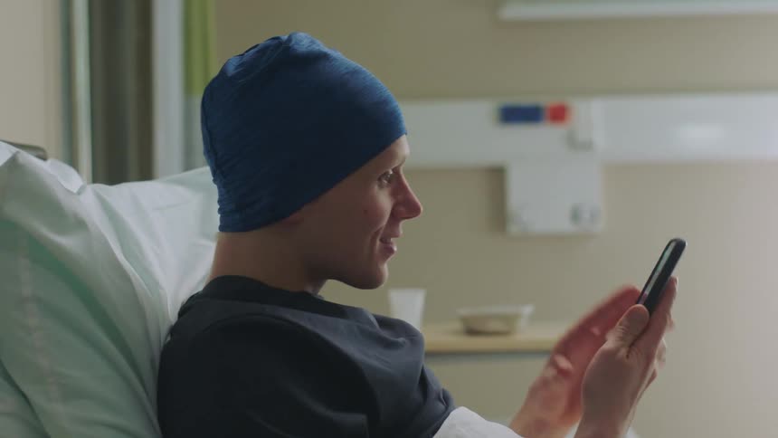 A man is sitting in a hospital room and looking at a cellphone