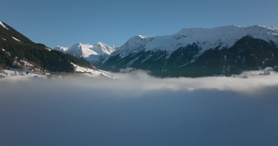 Fog is on the ground and snow covered mountains are in the distance under a clear blue sky