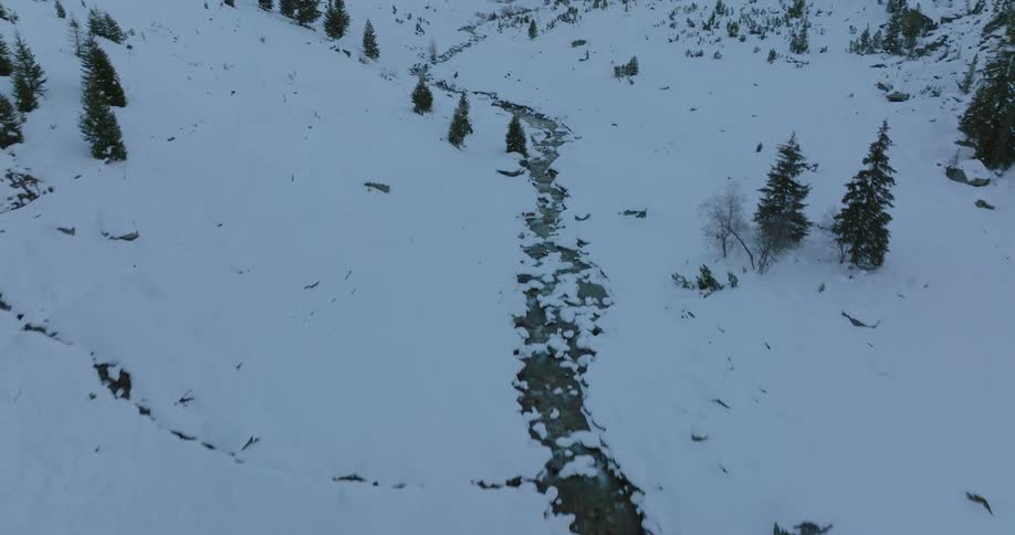 A stream runs through a snow covered valley as the sun shines brightly on the mountainside