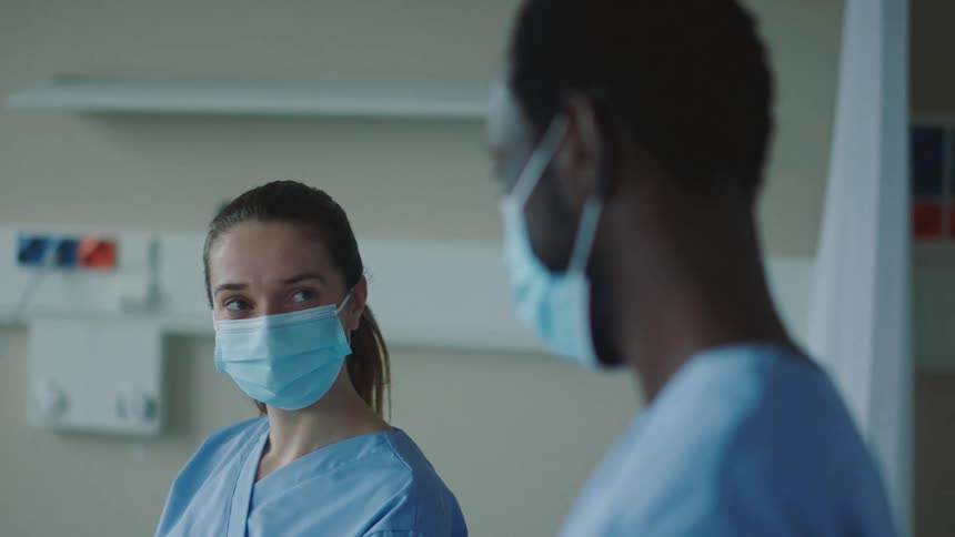 A male and female nurse in face masks looking at each other in a hospital room