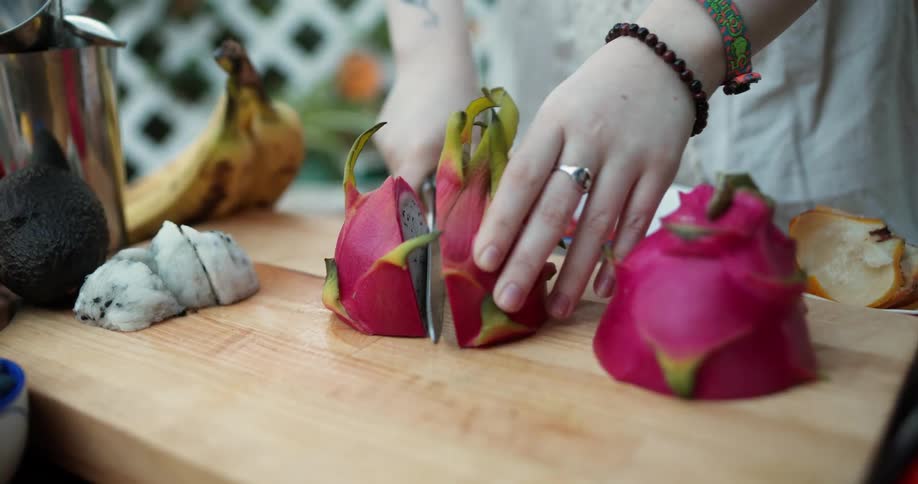 A woman cutting a dragon fruit on a wood cutting board