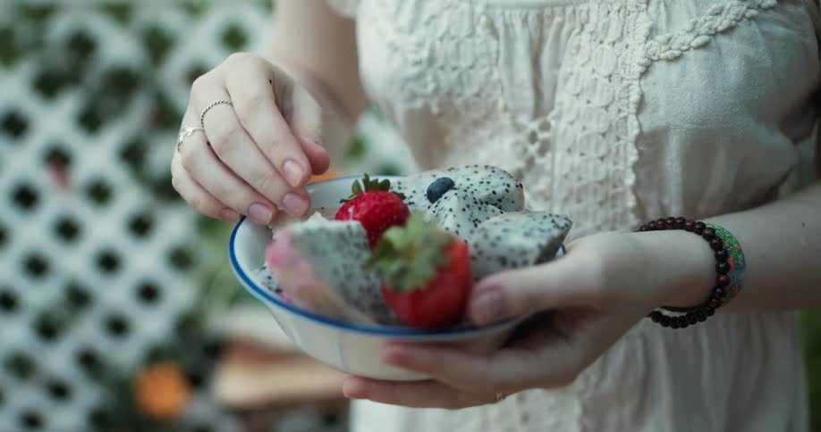 A woman with shaky hands putting fruit into a ceramic bowl outside in the summer
