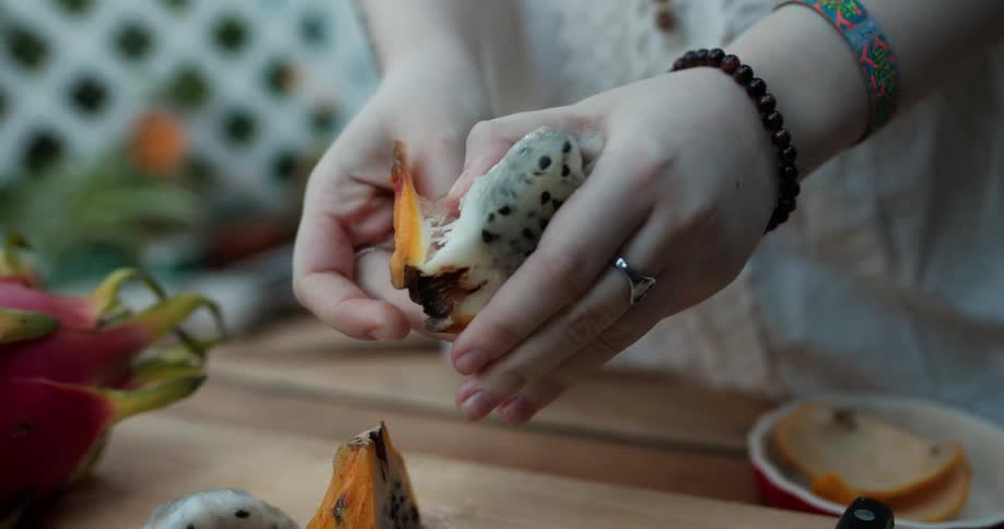 A woman peels the thick skin off a dragonfruit