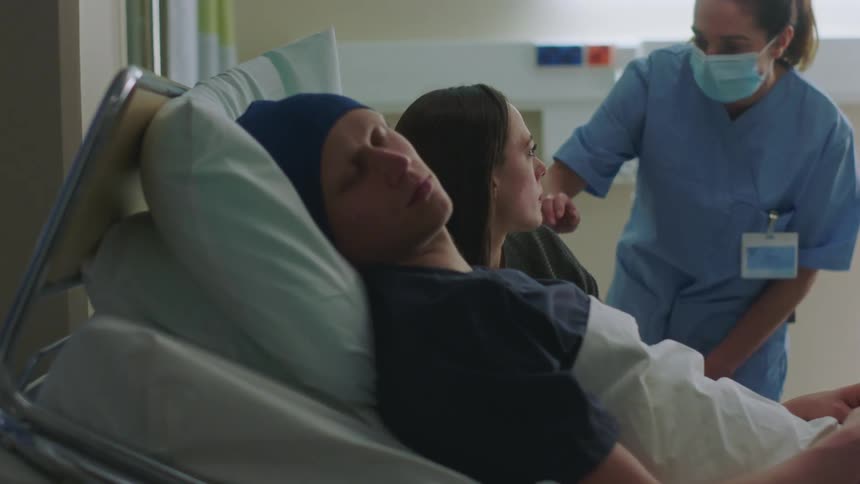 A woman sleeps in a hospital bed with a man when the nurse wakes her up to give medicine to the patient