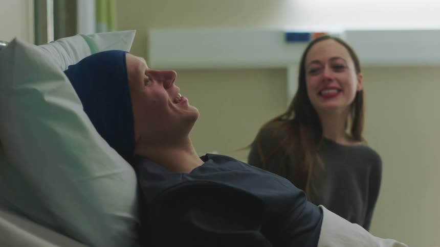 White man lying down at a hospital bed while talking and laughing with a woman sitting next to him