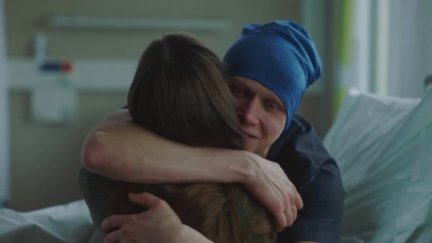 Patient laying in a hospital bed hugs his partner after receiving good news