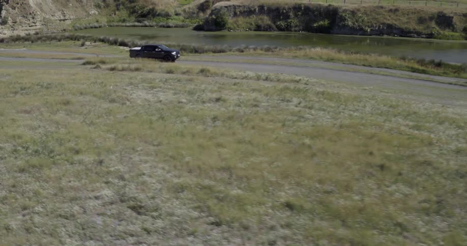 A car is driving near the water by a grass field
