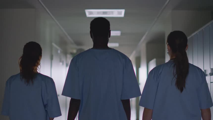 Nurses wear scrubs and face masks while walking down hospital corridor
