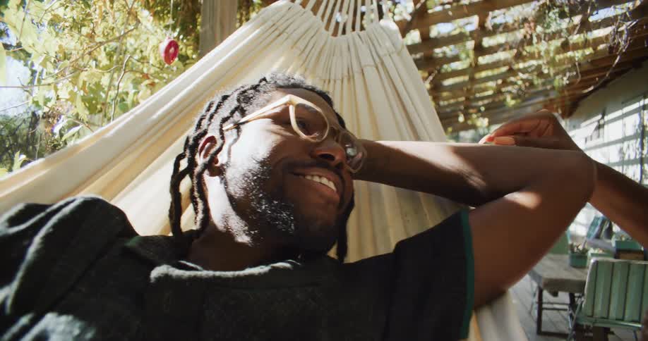 A man lies on a hammock on a porch and smiles as a woman strokes his arm