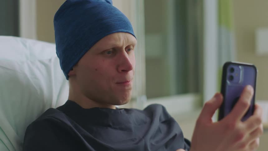 A man in a hospital bed puts his phone down and tries not to cry after a video call
