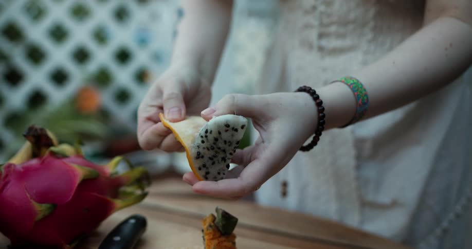 Young pale woman peeling the skin of a slice of dragon fruit over a table outdoors