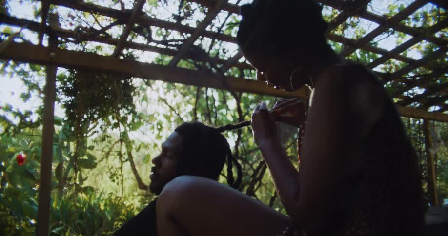 Woman braids the dreadlocks on her partner head sitting in the porch at morning
