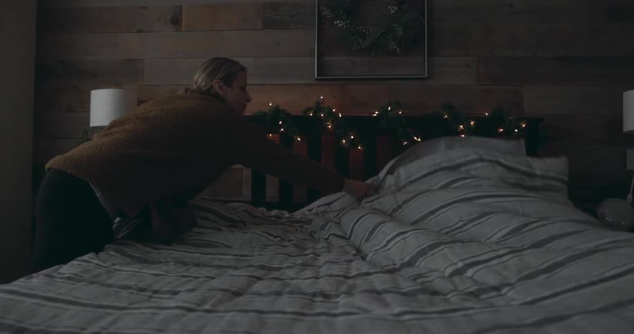 A woman spreads a comforter onto a bed with garland and fairy lights on its headboard