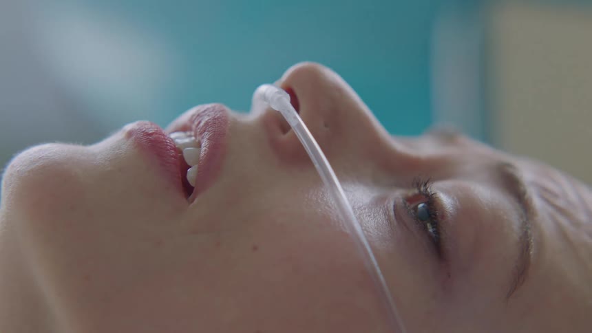 A woman with a breathing tube in her nose struggles to breathe