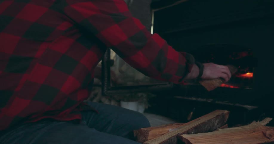 A man places cut firewood into a wood burning stove at home