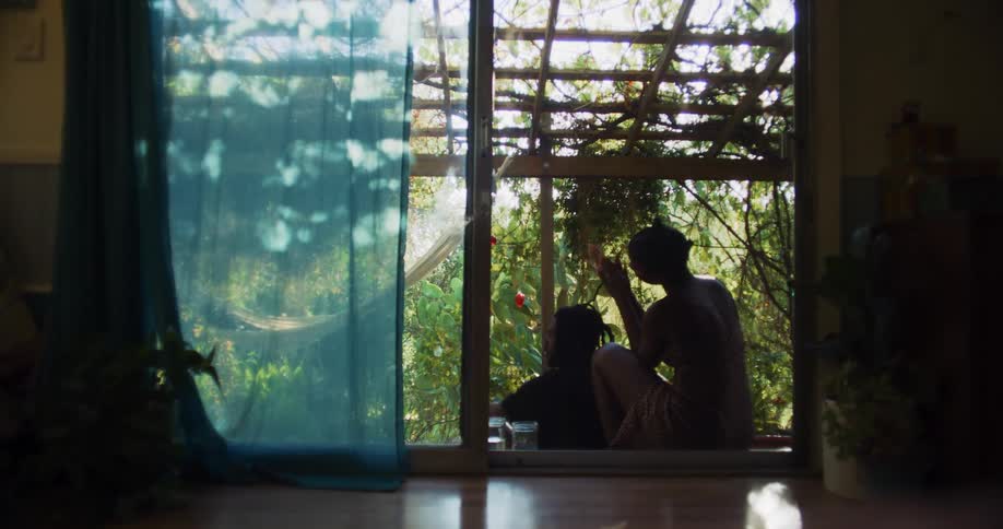 A woman sitting on a step above her husband braiding and fixing his long hair in the garden