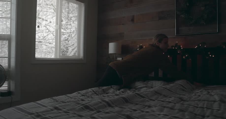 Woman makes bed near window