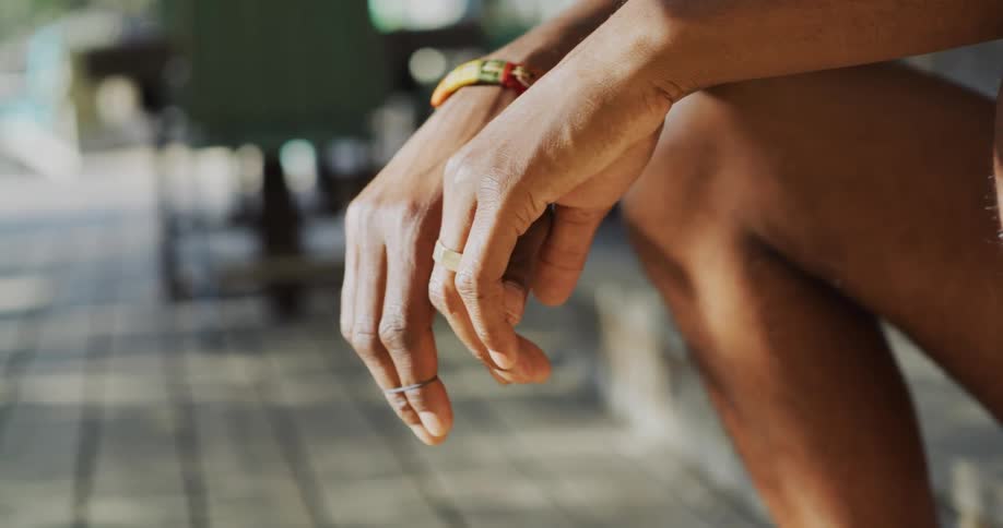 Close up of a mans hands and leg as he sits outside on a patio