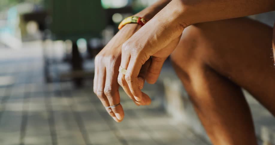Man with wristband and rings sits on stairs in the street
