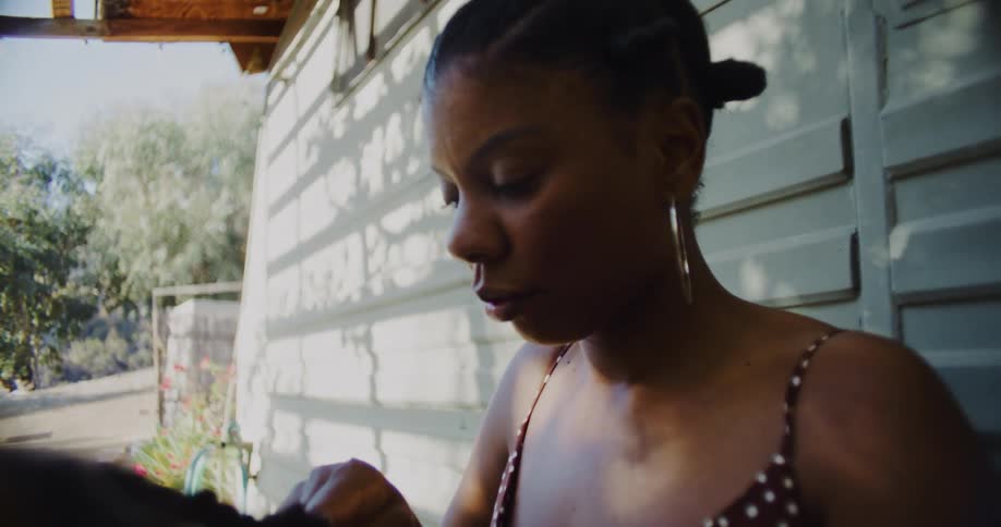 A woman on a porch braids a mans hair