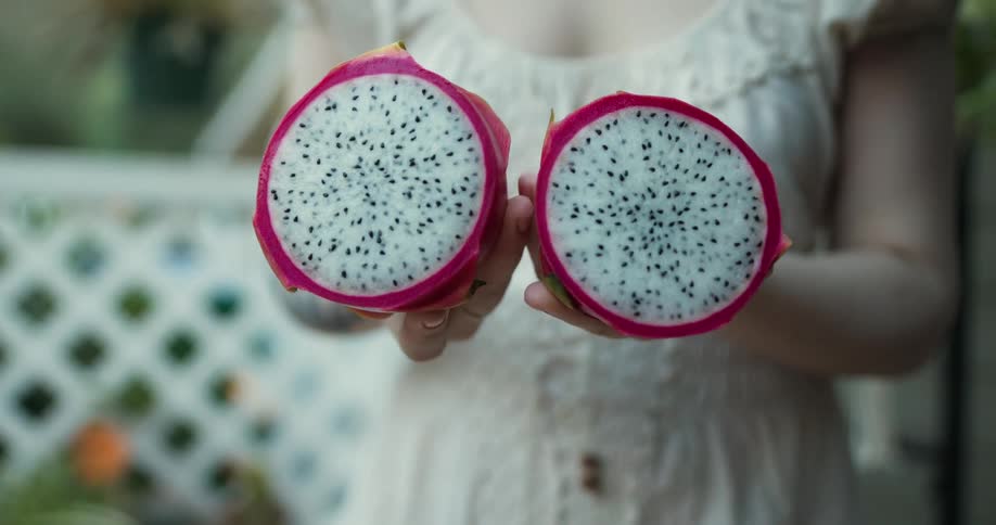A woman standing outside holds a dragon fruit sliced in half