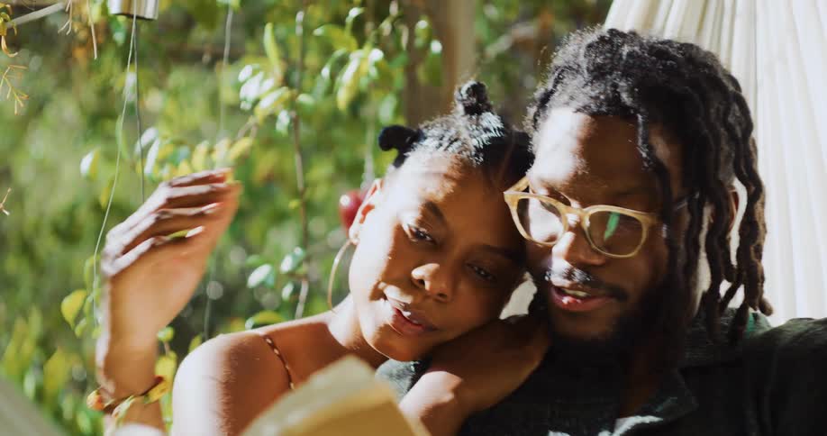 A couple llie in a hammock and read a book together