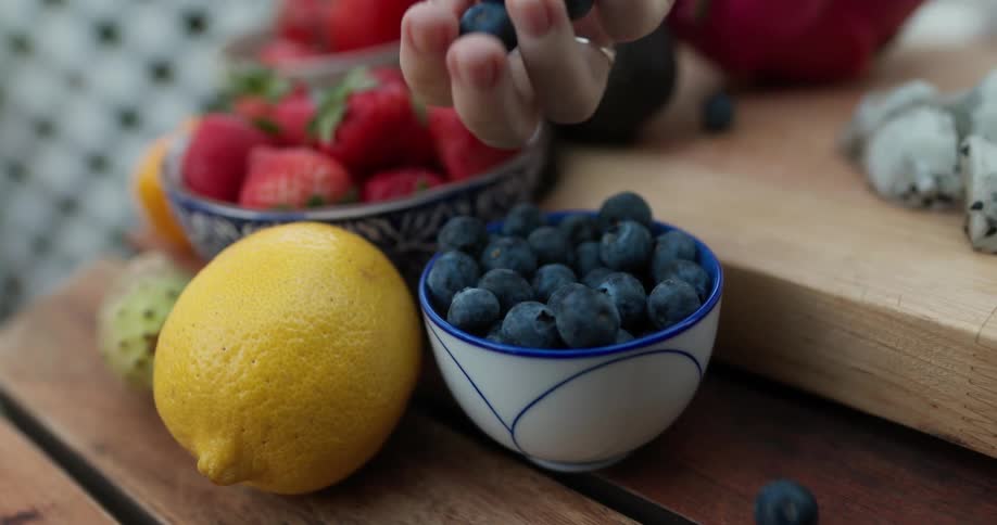 A woman picking up a handful of blueberries from a ceramic bowl