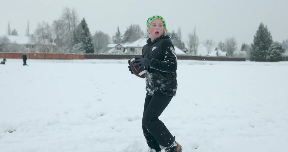 A teenage boy is outside in the snow playing football with his father