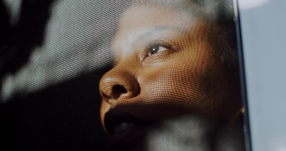 Woman leans close to window as she looks out through screen