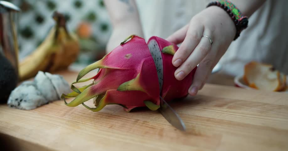 A woman cutting a dragon fruit in half on a wood cutting board