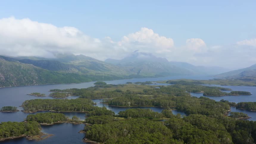 An aerial view of a lake with treed islands and hills in the background