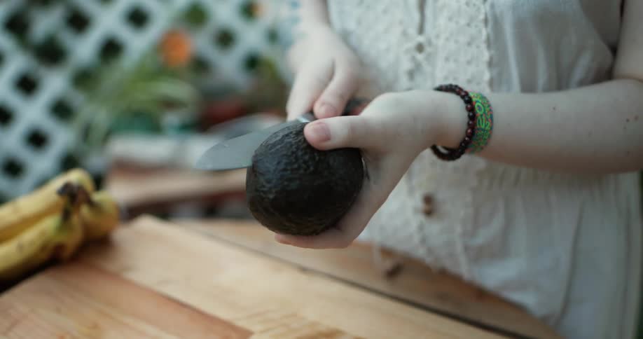 A woman cuts an avocado in half and looks at it
