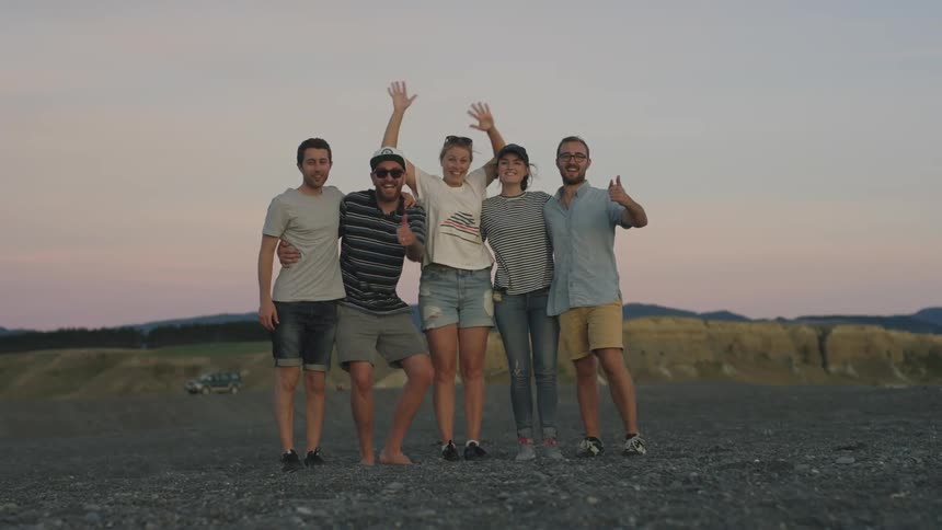A group of people standing outside embrace and wave as they pose for a photo