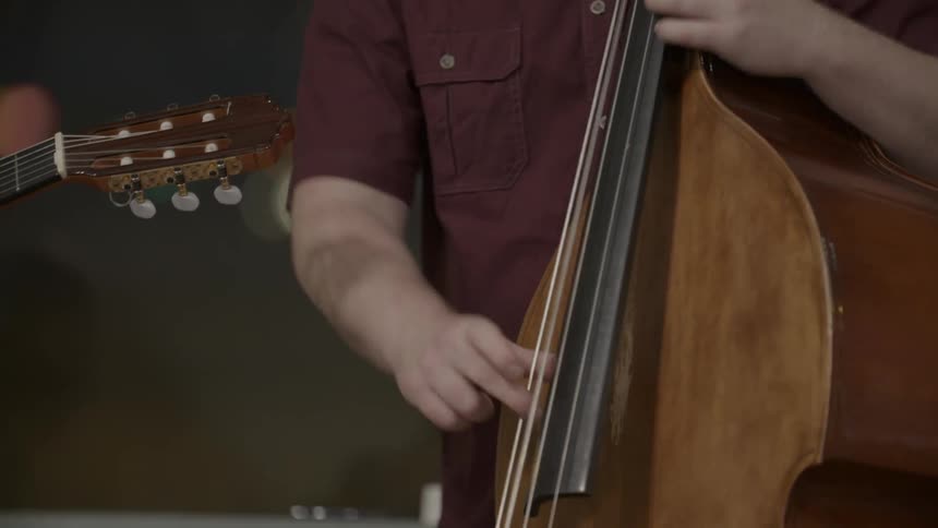 A man plays a standing bass and some else has a guitar