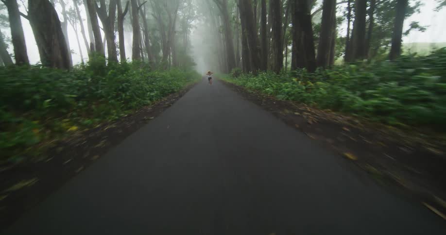 A woman wearing shorts and is holding her sun hat as she runs on a forest road