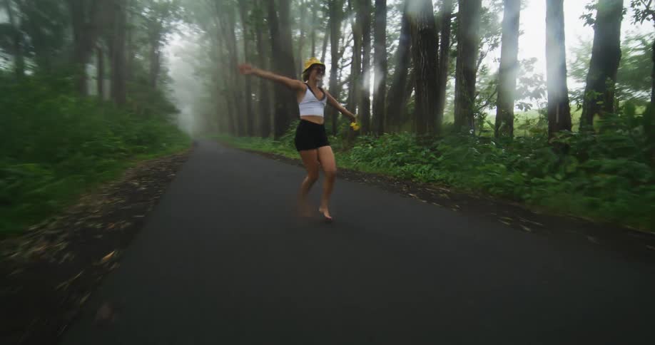 Woman with hat white sleeveless shirt and black shorts happily walks on forest road in fog