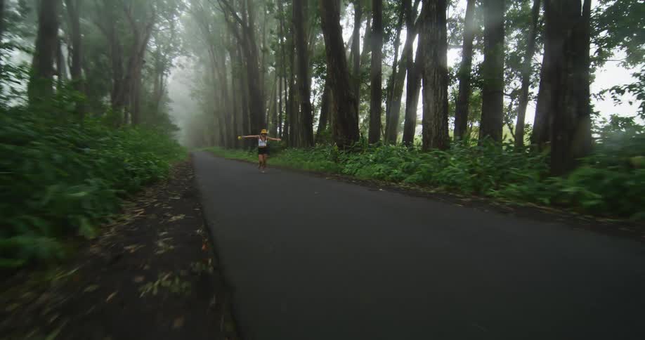 Woman with hat white sleeveless shirt and black shorts happily walks on forest asphalt road in fog
