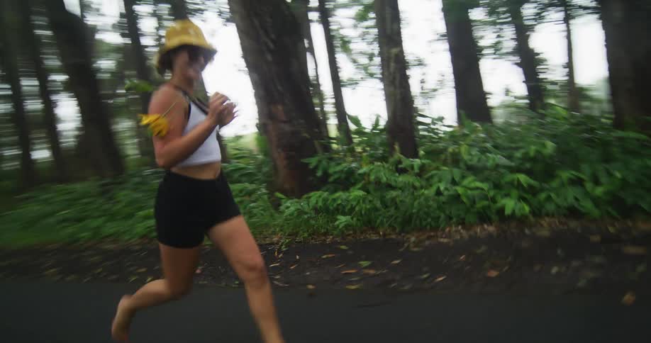 A woman wearing shorts and a sun hat is running on a forest road