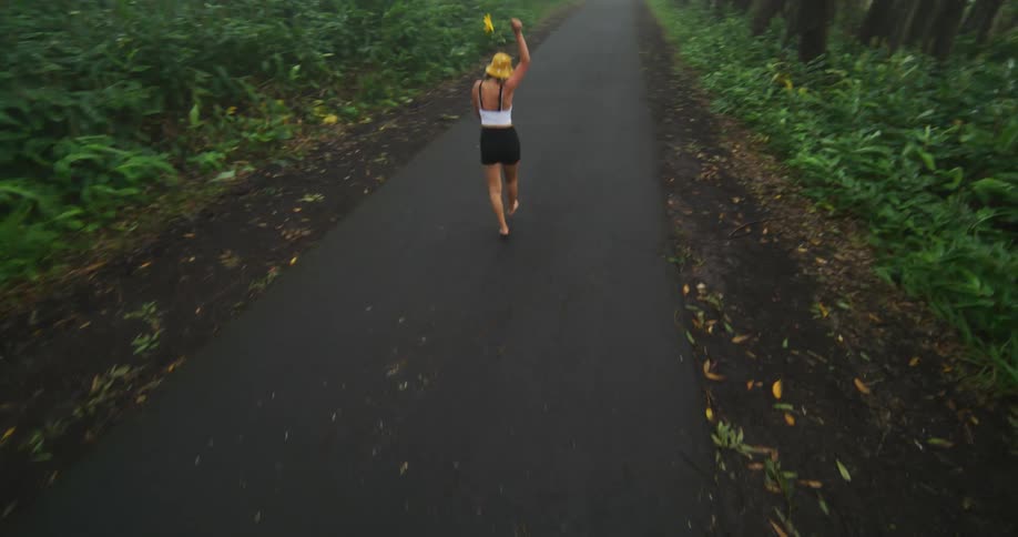 Woman with hat white sleeveless shirt and black shorts happily walks on forest road in fog