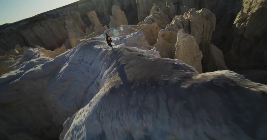 A person walks along a narrow ridge with jagged rocks cliffs and canyon below