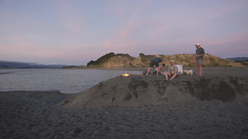 A group of friends and a small dog relax on a mound near a shoreline