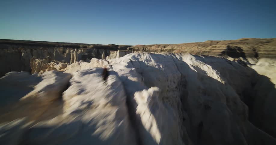Hiker moves across ridge in rough terrain bordering flat plain