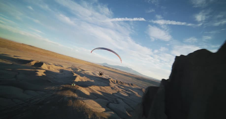 A person parachutes into the middle of a desert near a tall formation