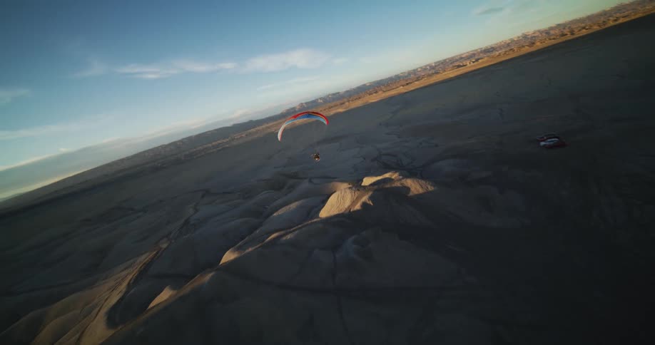 A paraglider flies over sand dunes in the desert