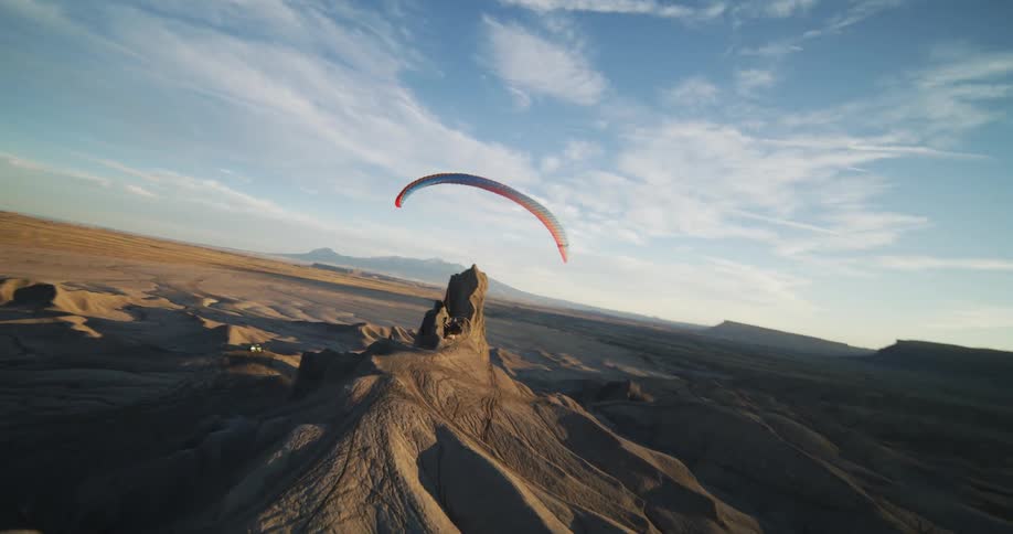 A hang glider floats over the desert dunes and rock formations
