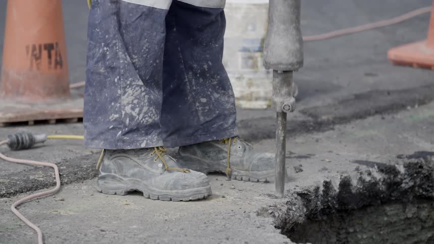 A worker is using a jackhammer on a street