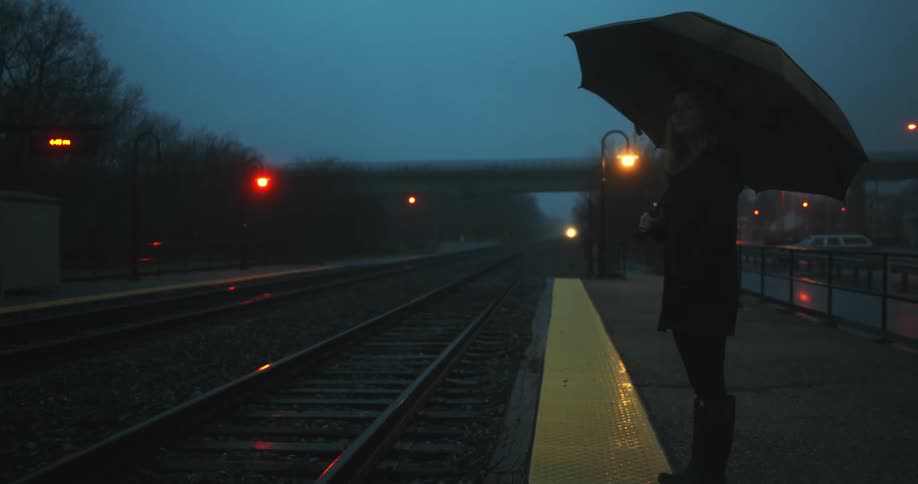 A woman stands under an umbrella as she waits for a train to come