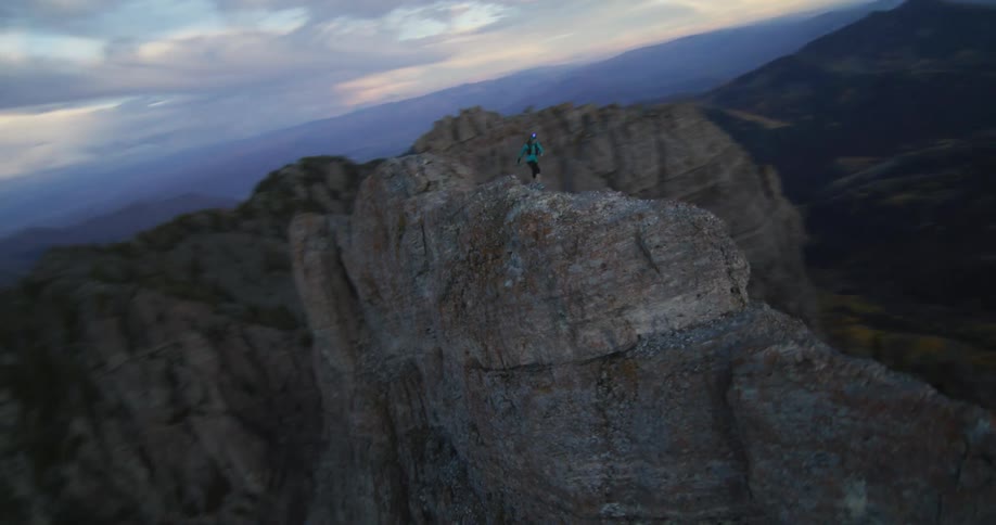 Hiker moves along ridge to stand at edge with their arms spread