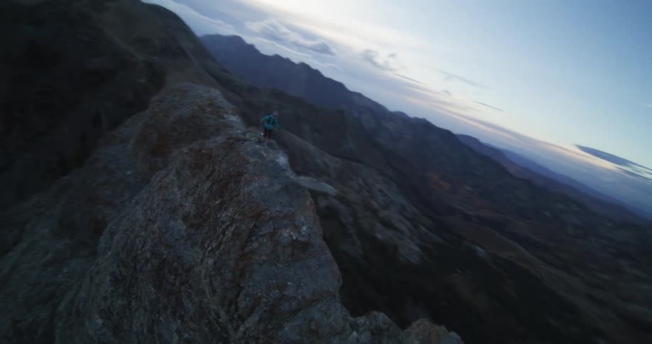A woman runs across the narrow peak of a mountain